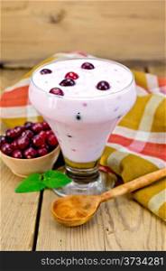 Thick yogurt in glass with cranberries, spoon, napkin, cranberries in a bowl, mint on a wooden boards background