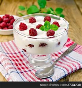 Thick yogurt in glass with raspberries and spoon on a napkin, raspberries in the bowl, mint on the background of wooden boards