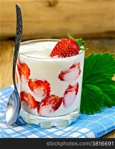Thick yogurt with strawberries in a glass with a spoon and leaves napkin on a wooden boards background