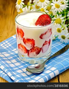 Thick yogurt with strawberries in a glass with a spoon, napkin, a bouquet of daisies on a background of wooden boards