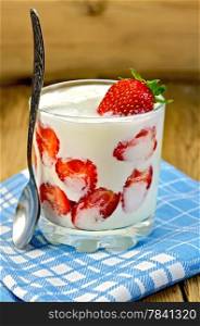 Thick yogurt with strawberries in a glass with a spoon, napkin on the background of wooden boards