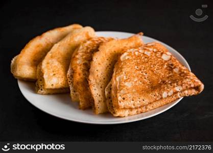 Thin pancakes on a plate on a black background. Traditional Russian food.. Thin pancakes on a plate on a black background, traditional Russian food.