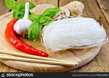 Thin rice noodles with garlic, red pepper, ginger, basil, chopsticks on a wooden boards background