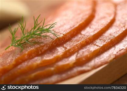 Thin smoked salmon slices with garnished with dill on wooden board (Selective Focus, Focus in the middle of the image). Smoked Salmon with Dill