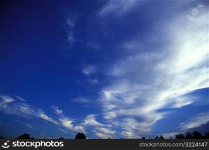 Thin White Clouds In A Clear Blue Sky Over Trees