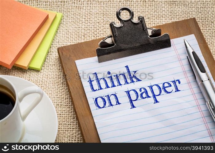 think on paper - write down your goals,tasks and ideas - text on clipboard with a pen, coffee and sticky notes against burlap canvas