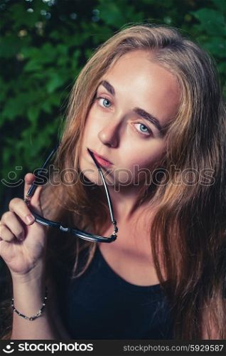 Thinkful blonde looking at camera and holding her glasses in her hand