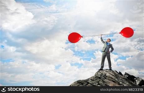 Thinking he is strong. Confident businessman lifting above head barbell with balloons