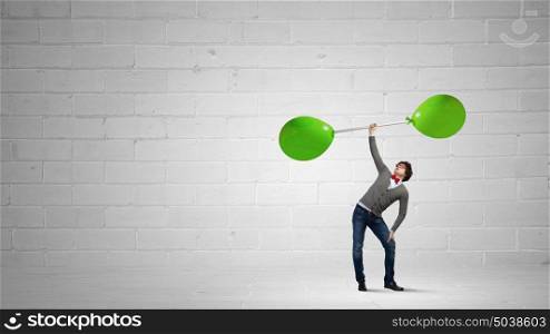 Thinking he is strong. Confident businessman lifting above head barbell with balloons