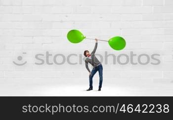 Thinking he is strong. Confident guy lifting above head barbell with balloons