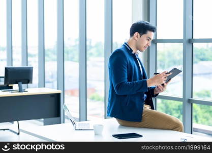 Thinking of asian young businessman working with read the note recorded in the business plan notebook and laptop computer,smartphone sit on the table In the office room background.