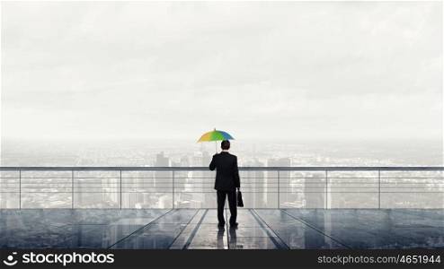 Thinking optimistic. Businessman standing with back on building roof with colorful umbrella