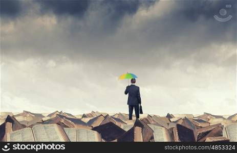 Thinking optimistic. Businessman standing with back on pile of old books with colorful umbrella