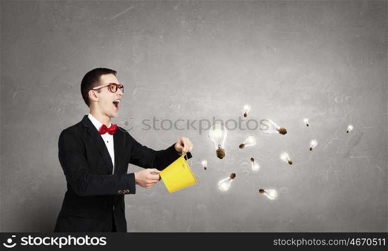 Thinking outside the box. Young funny guy wearing jacket splashing bulbs from yellow bucket