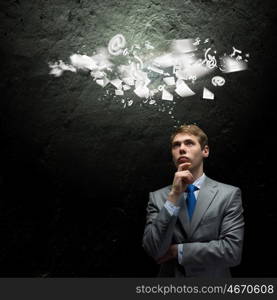 Thinking over an idea. Young thoughtful businessman looking up with hand on chin