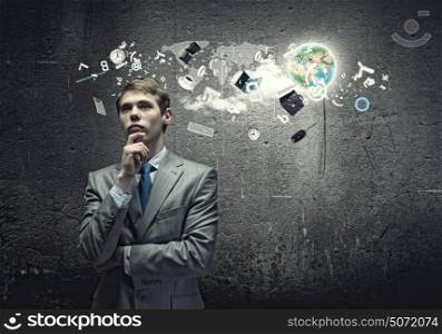 Thinking over an idea. Young thoughtful businessman looking up with hand on chin. Elements of this image are furnished by NASA