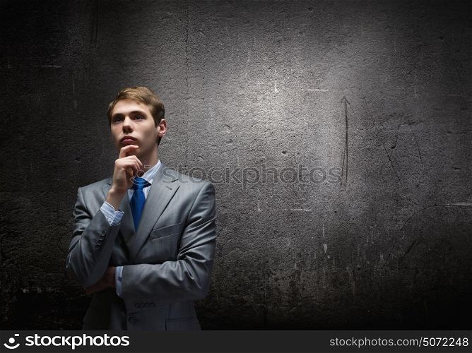 Thinking over an idea. Young thoughtful businessman looking up with hand on chin