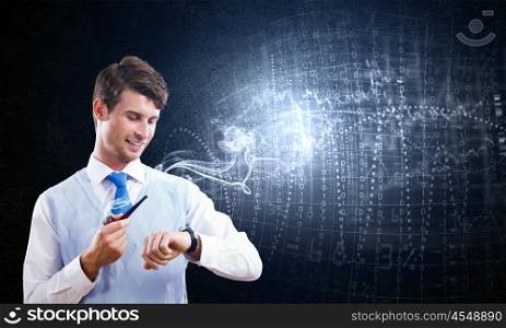 Thinking over the idea. Young businessman smoking pipe with diagrams and graphs at background