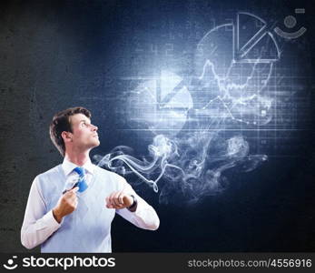 Thinking over the idea. Young businessman smoking pipe with diagrams and graphs at background