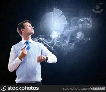 Thinking over the idea. Young businessman smoking pipe with diagrams and graphs at background