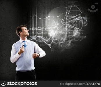 Thinking over the idea. Young businessman smoking pipe with diagrams and graphs at background