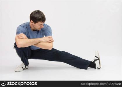 thirty young athletic man does physical exercises. Athlete crouching stretches muscles of left leg