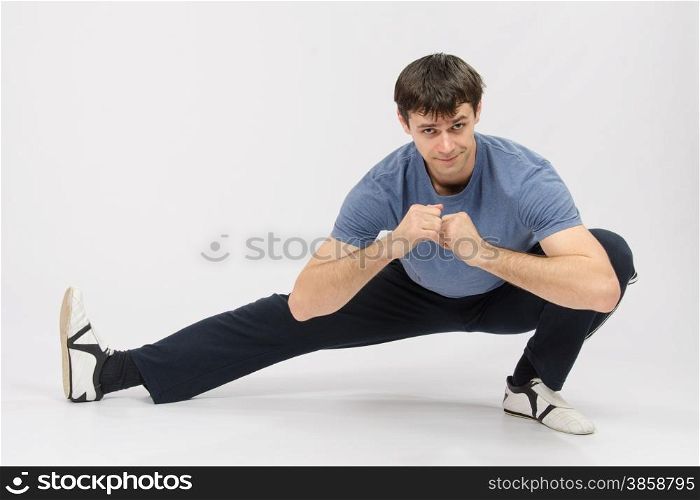 thirty young athletic man does physical exercises. Athlete crouching stretches the muscles of right leg