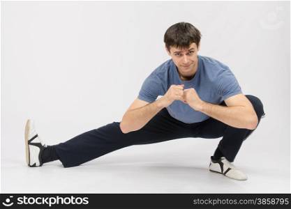 thirty young athletic man does physical exercises. Athlete crouching stretches the muscles of right leg