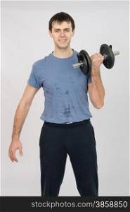thirty young athletic man does physical exercises. Athlete dumbbell raises his left hand
