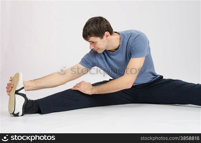 thirty young athletic man does physical exercises. Athlete in training stretches the muscles of right leg