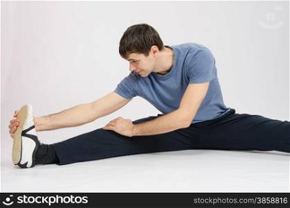 thirty young athletic man does physical exercises. Athlete in training stretches the muscles of right leg