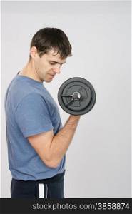 thirty young athletic man does physical exercises. Athlete looks at arm muscles under weight of dumbbell
