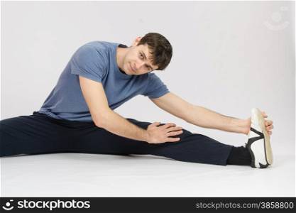 thirty young athletic man does physical exercises. Athlete stretches the muscles of left leg