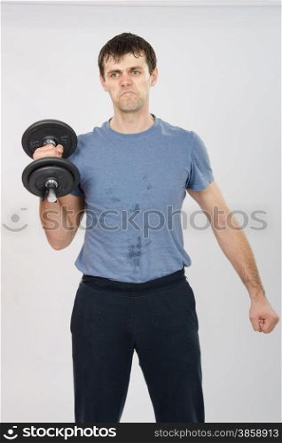 thirty young athletic man does physical exercises. athlete with a dumbbell effort raises his right hand