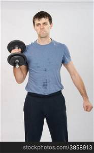 thirty young athletic man does physical exercises. athlete with a dumbbell effort raises his right hand