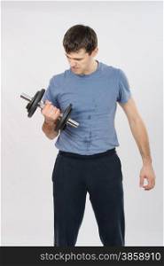 thirty young athletic man does physical exercises. athlete with a last effort raises dumbbell