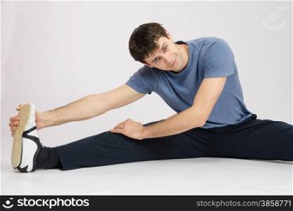 thirty young athletic man does physical exercises. Man in training stretches muscles of the right leg