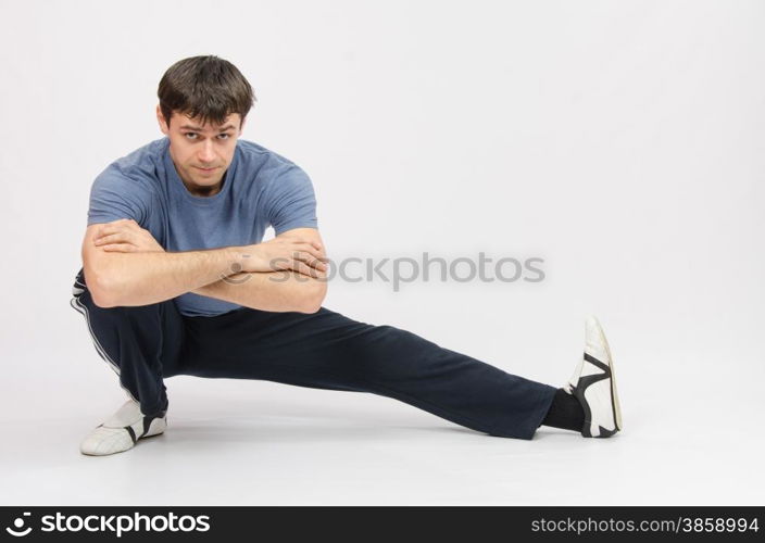 thirty young athletic man does physical exercises. Sportsman squatting muscles pulling the left foot