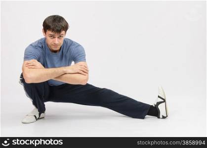 thirty young athletic man does physical exercises. Sportsman squatting muscles pulling the left foot