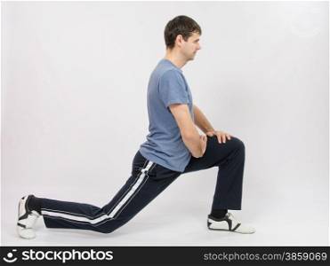 thirty young athletic man does physical exercises. The athlete performs stretching using squats