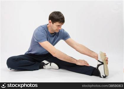 thirty young athletic man does physical exercises. The young man stretches muscles of left leg