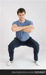 thirty young athletic man does physical exercises. young man performs squats