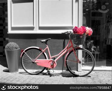 This vintage pink girls bicycle has beautiful pink flowers in a basket on the front of the bike