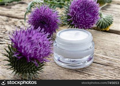 Thistle flower with open jar of cosmetic face cream on wooden background. Medicinal plant. Natural cosmetic.. Thistle flower with open jar of cosmetic face cream on wooden background. Medicinal plant.