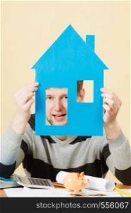 Thought about house new flat. Young handsome positive man with paper model of real estate. Smiling guy dreaming thinking about his own place to live.. Young man with paper model of house.