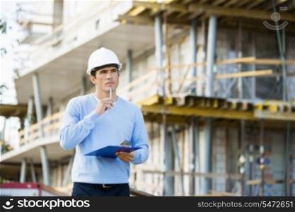 Thoughtful architect with clipboard and pen standing at site