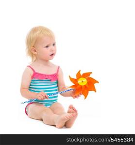 Thoughtful baby in swimsuit with pinwheel sitting on floor