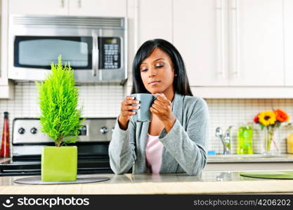 Thoughtful black woman holding coffee mug in modern kitchen interior
