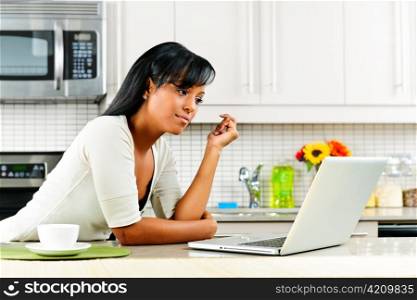 Thoughtful black woman using computer in modern kitchen interior
