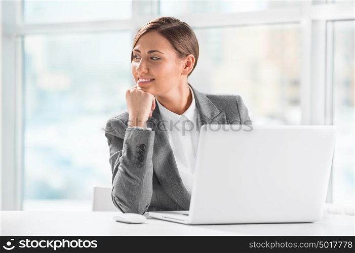 Thoughtful business woman holding chin while using laptop at work